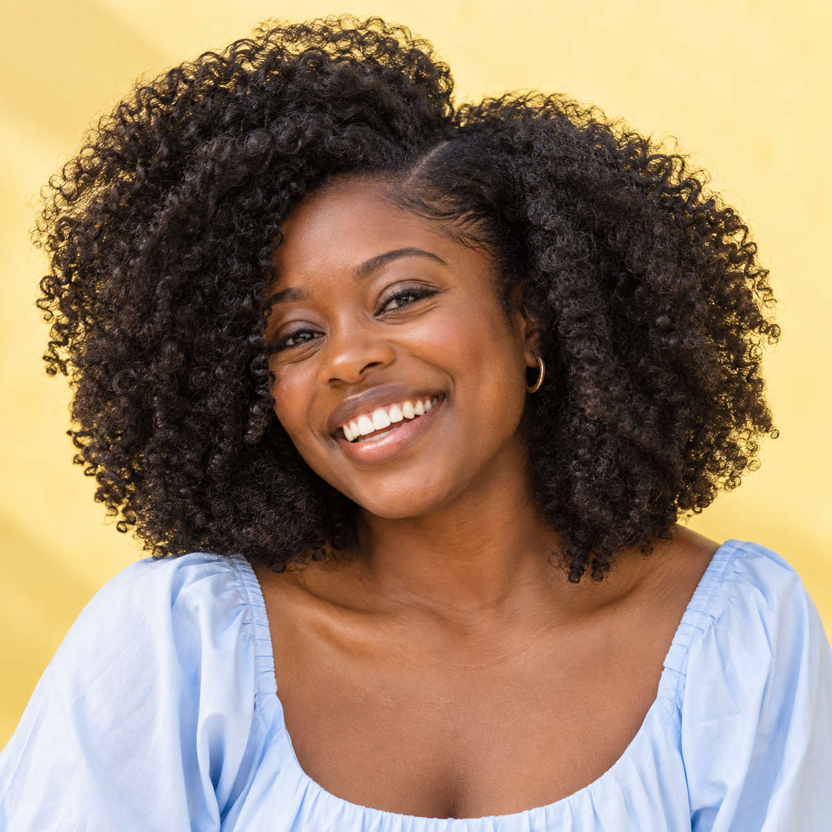 Smiling woman with voluminous natural coils against a sunny yellow background